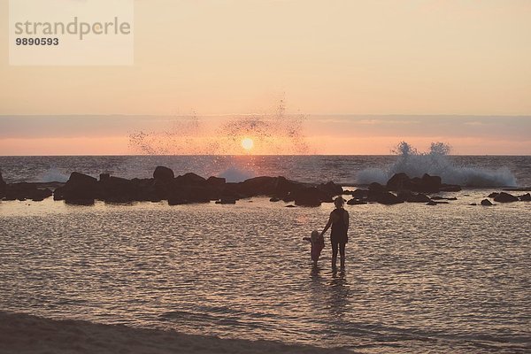 Silhouettierte Mutter und Kleinkind beim Paddeln im Meer mit Blick auf spritzende Wellen  Kona  Hawaii  USA