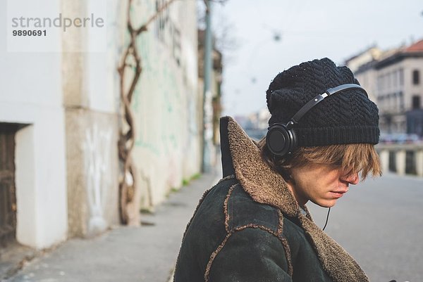Mann hört Musik über Kopfhörer am Bordstein  Mailand  Italien