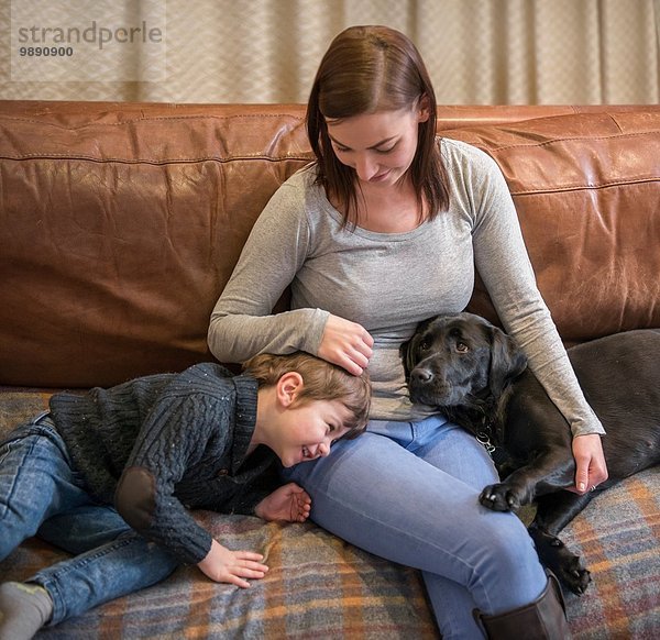 Mutter und Sohn entspannen auf dem Sofa zu Hause mit Haustier Labrador