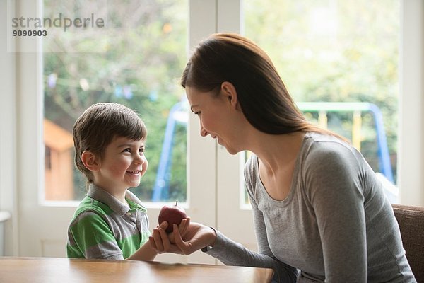 Junge lächelt Mutter an  als er ihr den Apfel gibt.