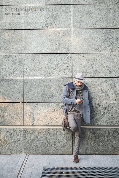 Geschäftsmann lehnt sich an die Wand SMS auf dem Smartphone