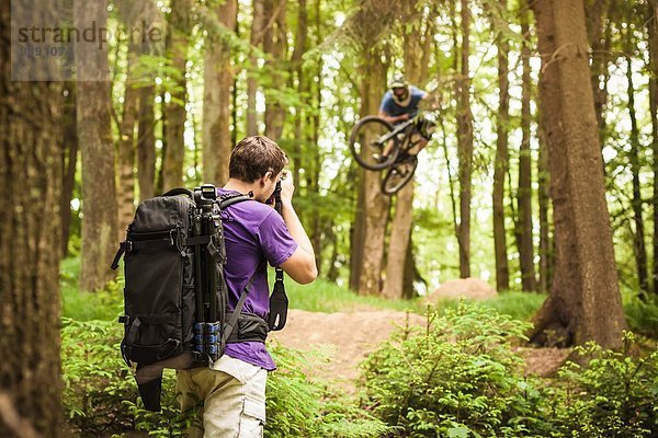 Junger Fotograf fotografiert Mountainbiker im Wald