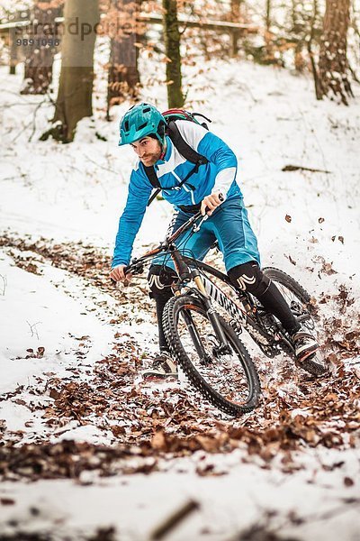 Junge männliche Mountainbiker  die auf verschneiten Waldwegen rasen