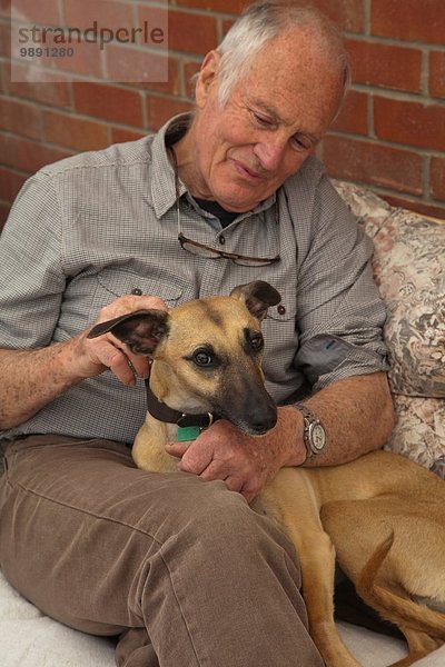 Älterer Mann  sitzend  streichelnder Hund