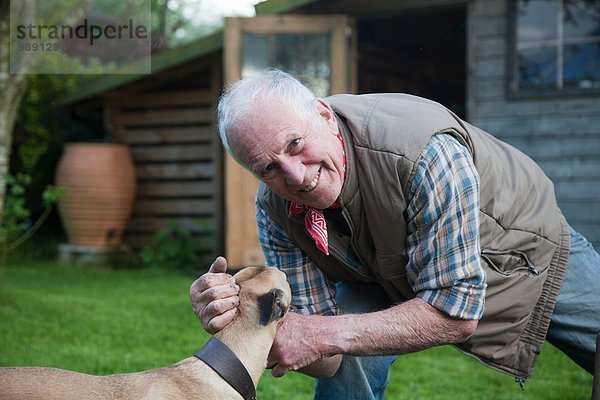 Senior Mann  streichelnder Hund im Garten