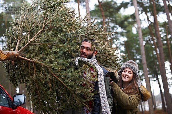 Junges Paar mit Weihnachtsbaum auf den Schultern im Parkhaus