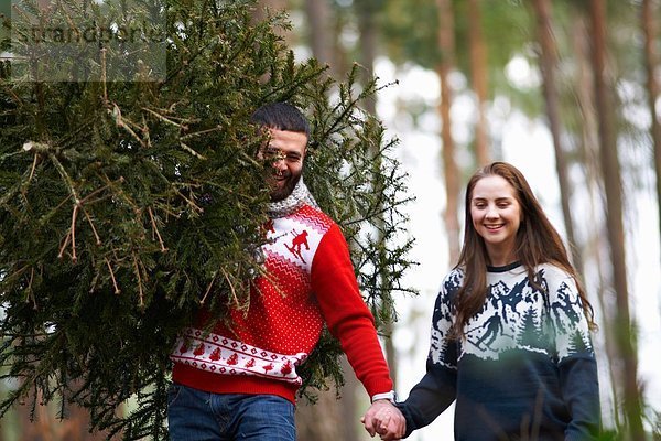 Junges Paar mit Weihnachtsbaum auf den Schultern im Wald