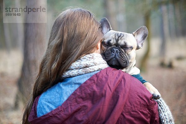 Porträt eines süßen Hundes  der von einer jungen Frau durch den Wald getragen wird.