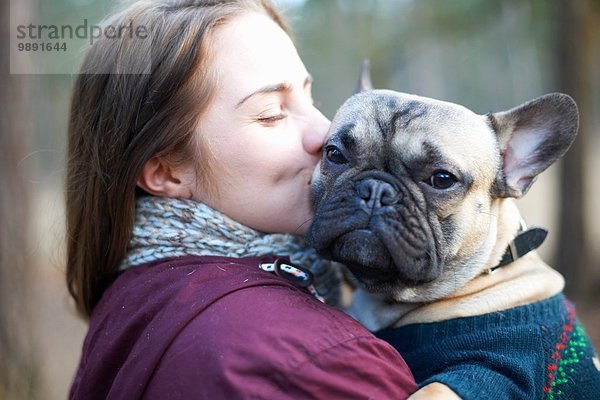 Porträt eines weisen Hundes  der von einer jungen Frau durch den Wald getragen wird.