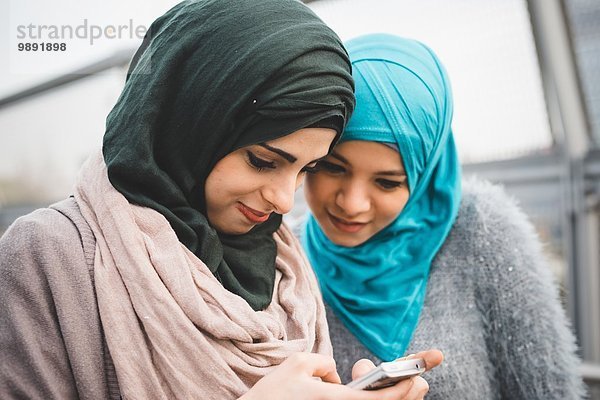 Zwei junge Freundinnen beim Lesen von Smartphone-Texten auf dem Parkweg