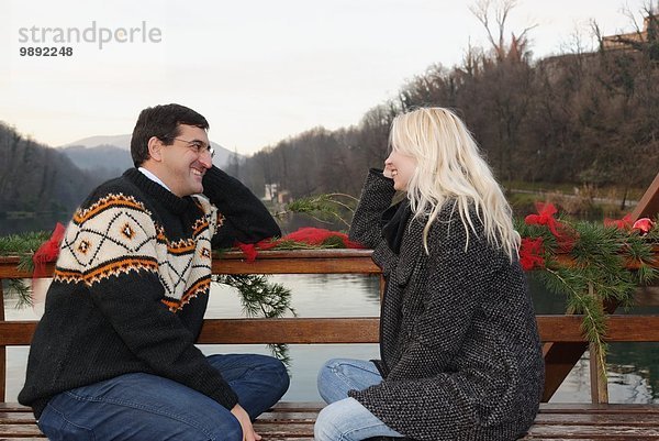 Heterosexuelles Paar sitzend von Angesicht zu Angesicht auf Bank  am See  Lombardei  Italien