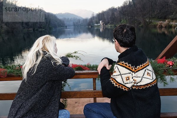 Heterosexuelles Paar auf Bank sitzend  am See  Blick auf die Lombardei  Italien