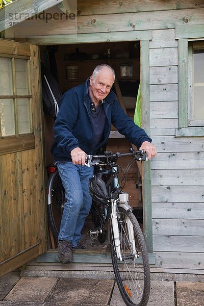 Älterer Mann auf dem Fahrrad bei Schuppen
