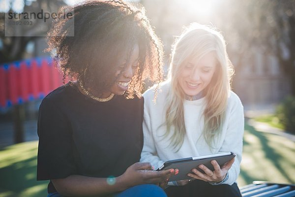 Zwei junge Freundinnen auf der Parkbank beim Betrachten des digitalen Tabletts  Como  Italien