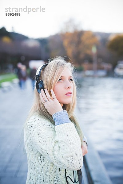 Junge Frau schaut auf und hört Kopfhörer am Seeufer  Como  Italien