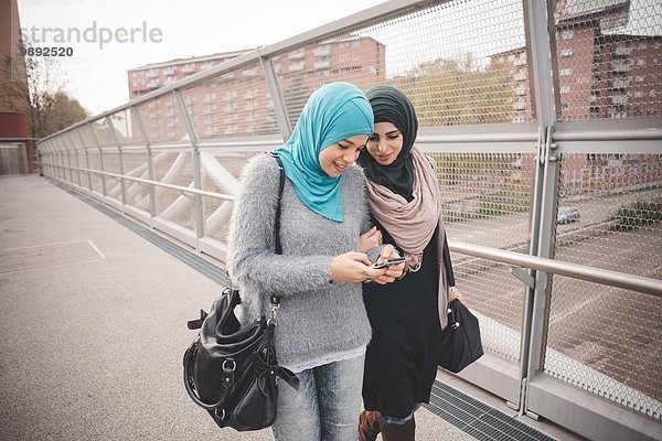 Zwei Freundinnen auf der Fußgängerbrücke beim Lesen von Smartphone-Texten