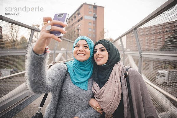 Zwei Freundinnen auf der Fußgängerbrücke nehmen Smartphone Selfie