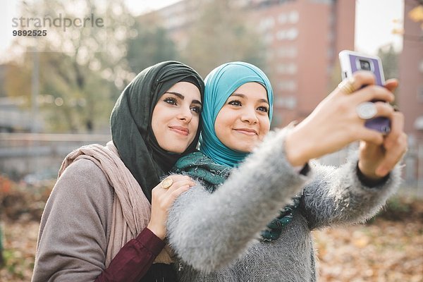Zwei Freundinnen im Park posieren für Smartphone Selfie