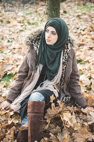 Junge Frau sitzend im Park zwischen Herbstblättern