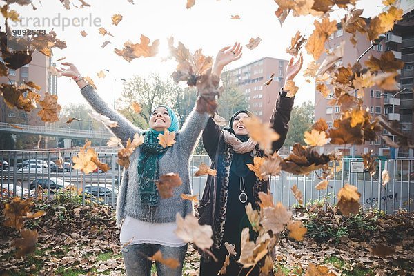 Zwei junge Frauen im Park beim Herbstlaubwerfen