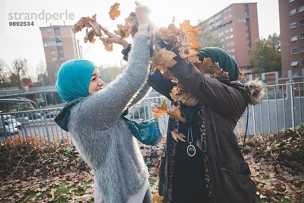 Zwei junge Frauen im Park spielen mit Herbstblättern.