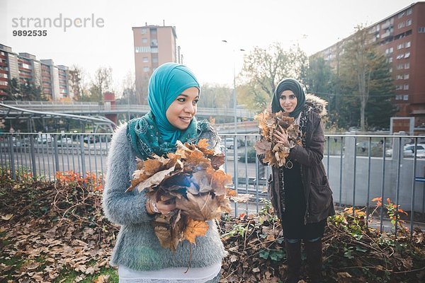 Zwei junge Freundinnen sammeln Herbstlaub im Park