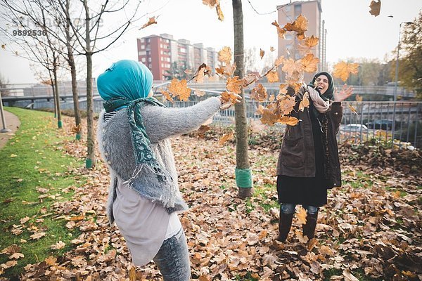 Zwei junge Frauen spielen im Park mit Herbstblättern.