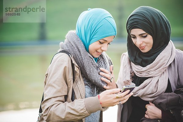 Zwei junge Frauen am Seeufer beim SMSen auf dem Smartphone