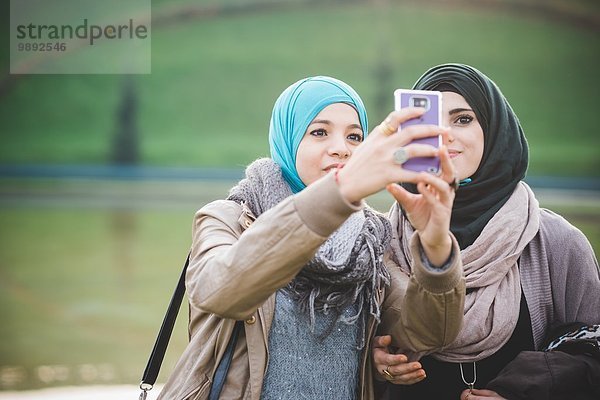 Zwei Freundinnen am Seeufer mit Smartphone-Selfie