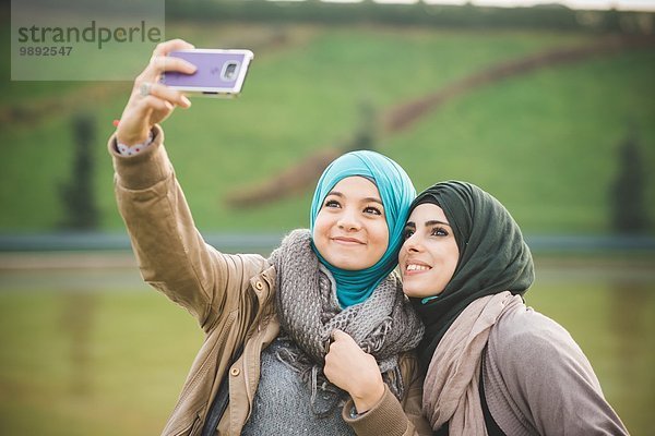 Zwei Freundinnen am Seeufer posieren für Smartphone Selfie