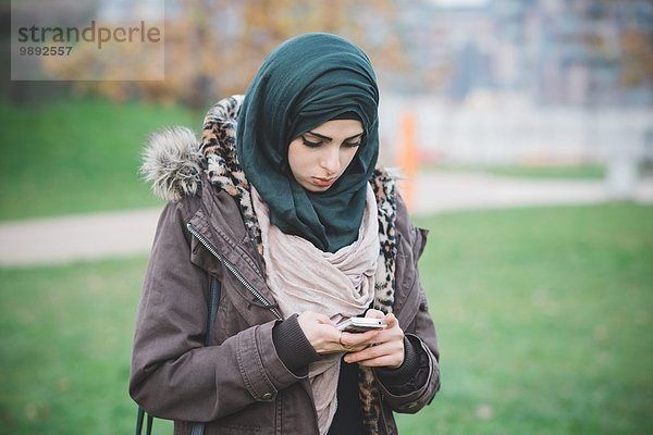 Junge Frau im Park SMS auf dem Smartphone