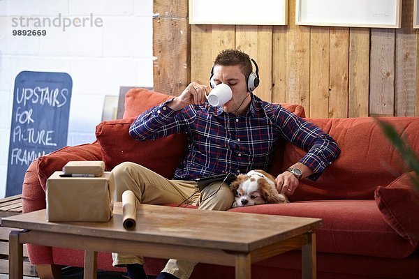 Mittlerer Erwachsener Mann trinkt Kaffee und streichelt Hund im Bilderrahmen-Showroom