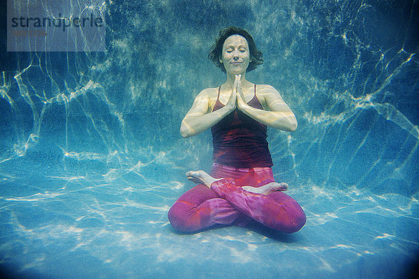 Reife Frau in roter Yogahose und Weste  in Yogastellung  Unterwassersicht