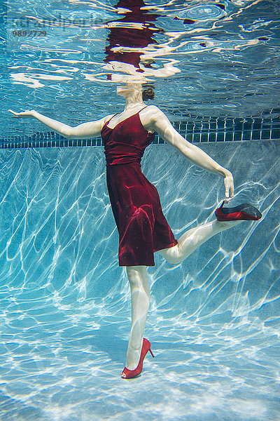 Reife Frau in rotem Kleid und High Heels  auf einem Bein stehend  Unterwasseransicht