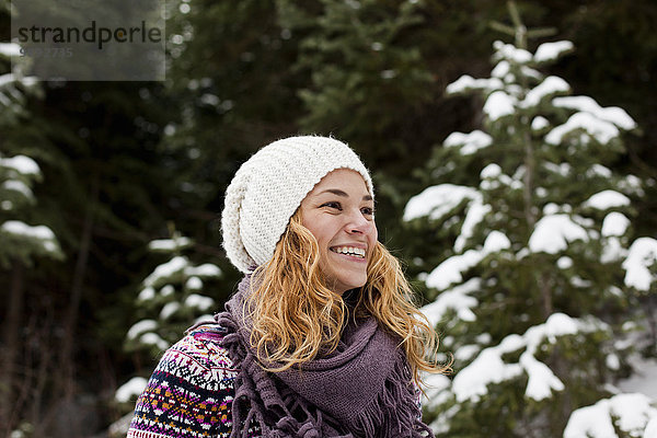 Porträt der lachenden jungen Frau vor schneebedeckten Tannenbäumen