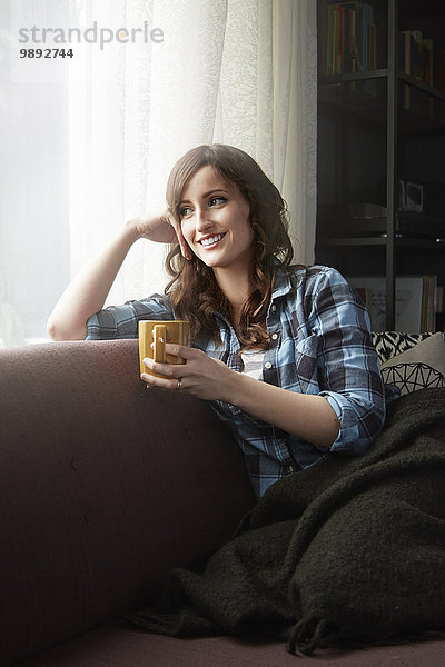 Junge Frau sitzt auf dem Sofa und trinkt Kaffee.