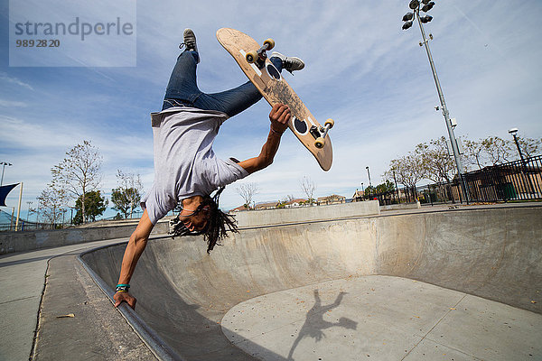 Junger Mann beim Skateboard-Trick verkehrt herum am Rande des Skateboard-Parks