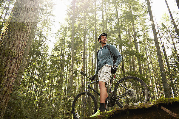Junger Mann stehend mit Mountainbike im Wald  Tiefblick
