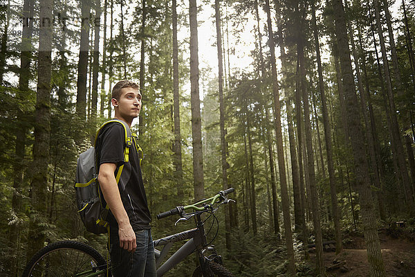 Junger Mann steht neben dem Mountainbike  im Wald