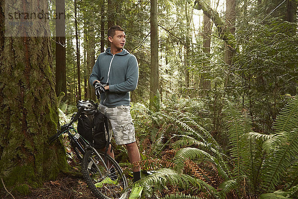 Junger Mann im Wald  lehnt Mountainbike gegen Baum