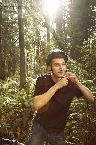 Junger Mann auf dem Fahrrad im Wald  Fahrradhelm sichern
