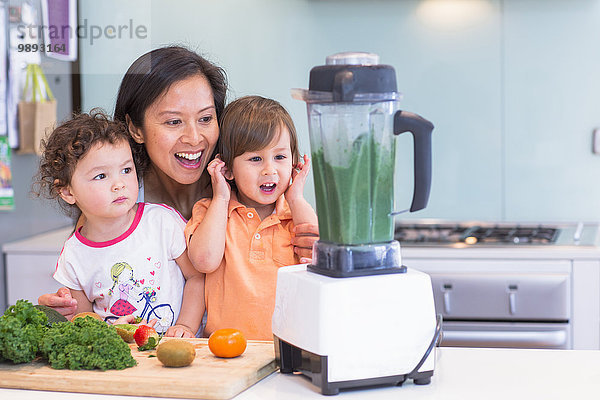 Mittlere erwachsene Frau macht Smoothie für zwei Kleinkinder in der Küche