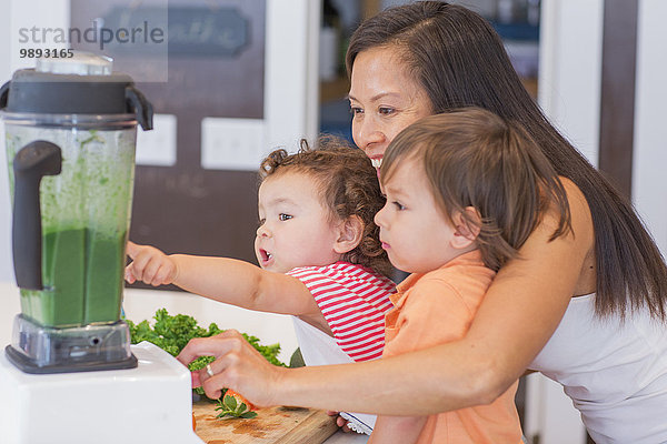 Mittlere erwachsene Frau macht grünen Smoothie für zwei Kleinkinder in der Küche