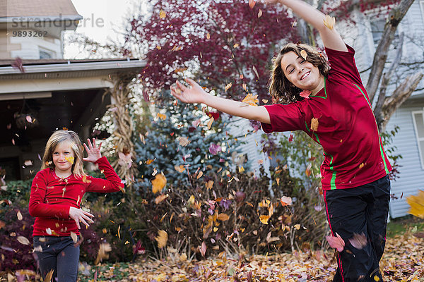 Geschwister spielen mit Herbstblättern im Garten