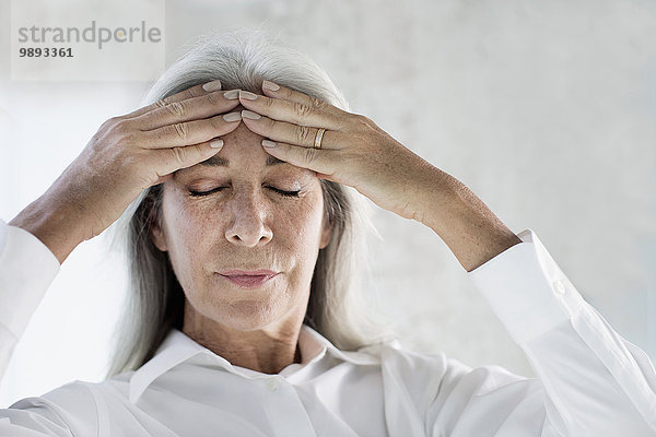 Portrait einer reifen Frau  die mit den Händen auf der Stirn meditiert.