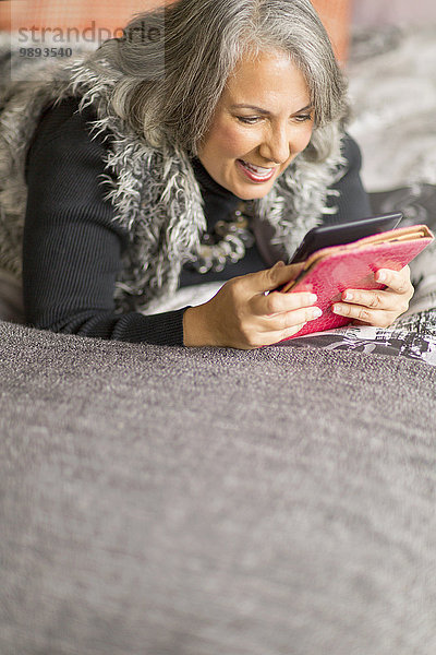 Reife Frau entspannt sich auf dem Bett  liest elektronisches Buch