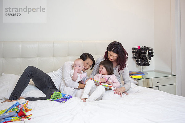Weibliches mittleres erwachsenes Paar  das mit Baby- und Kleinkindtöchtern auf dem Bett spielt.
