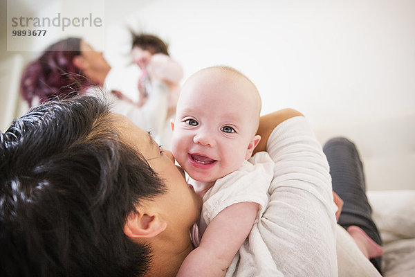 Über die Schulteransicht des weiblichen Paares auf dem Bett  das Baby- und Kleinkindtöchter umarmt.