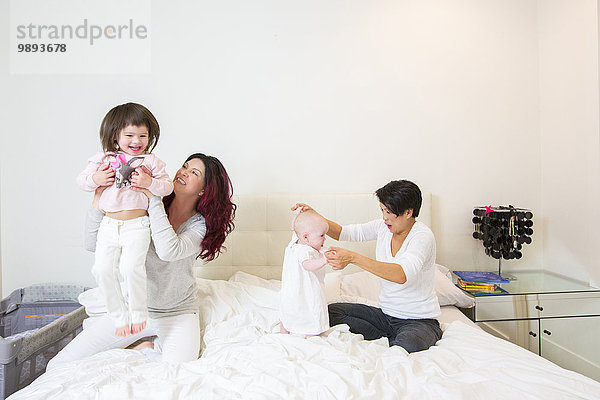Weibliches Paar im Bett  das sich mit Baby- und Kleinkindtöchtern amüsiert.