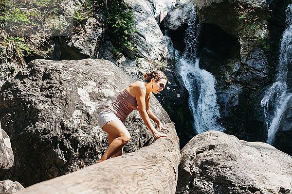 Eine Frau klettert auf einen Felsen in der Nähe eines Wasserfalls.